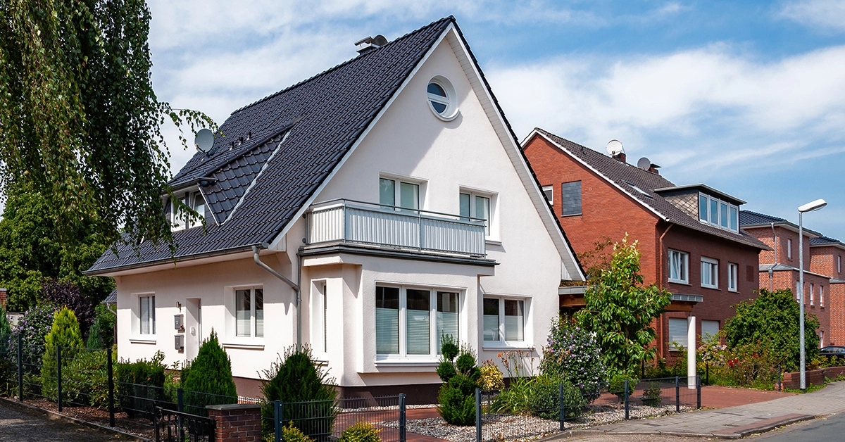 Weißes Einfamilienhaus mit dunklem Satteldach in einer Wohnstraße